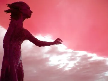 La madre del emigrante statue of a woman with an arm extended, silhouetted against a dramatic pink and white sky.