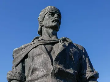 The Laçador bronze statue shows a man with a mustache and headband looking upward against a blue sky.
