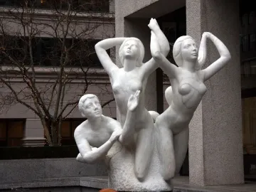 The Quest sculpture showing three marble nude figures outdoors, with a kneeling male figure and two women reaching upward.