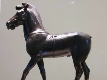 Bronze horse sculpture standing on a pedestal, facing left with clear support rods under the rear legs.