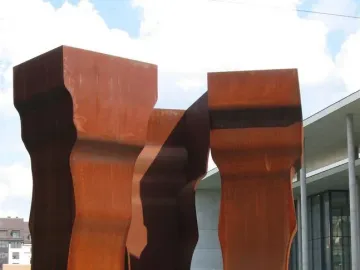 Buscando la Luz II sculpture with three tall rust-patinated metal forms on a grassy lawn.