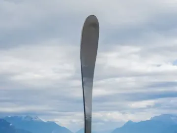 The Fork of Vevey sculpture stands upright in calm water with its reflection visible.