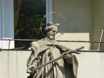 Stone statue of Saint John of Nepomuk holding a crucifix and palm frond, with a halo of stars.