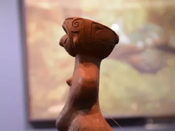 Jōmon Venus clay figurine shown in profile on a dark display surface.