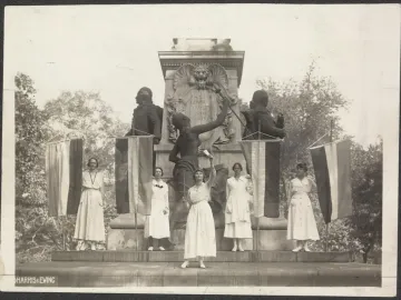Seven women stand on the steps of the Marquis de Lafayette statue, holding banners beside the monument.