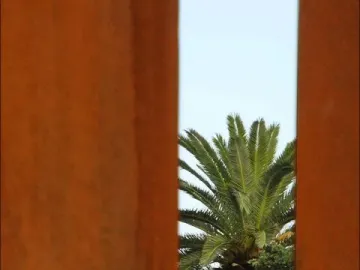 Two rusted metal columns frame a palm tree beneath the Neuf Lignes Obliques sculpture.