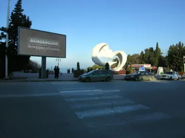 Peace Dove, a large white bird-like sculpture with spread wings in a park beside a street.
