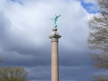 Battle Monument at West Point, a tall column topped by a winged female figure above small cannons and spheres.