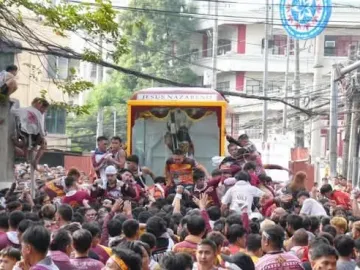 The Black Nazarene statue of Jesus in a decorated glass carriage moving through a crowd.