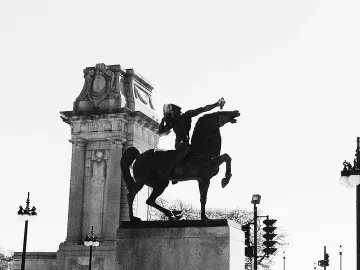 The Bowman sculpture silhouetted on a stone pedestal beside an ornate classical pillar.