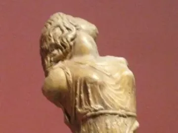 Dancing Maenad sculpture seen from behind, with the figure’s head tilted sharply upward and draped robes falling to the waist.