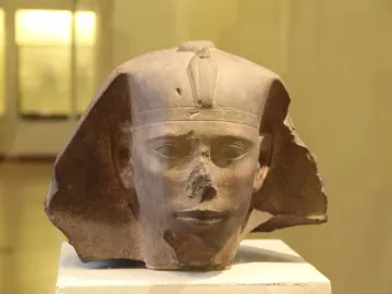Weathered stone head of the Djedefre sphinx with a damaged nose and royal headpiece featuring a cobra emblem.