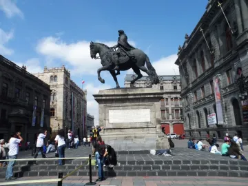 El Caballito equestrian statue on a stone pedestal in a public square surrounded by historic buildings and pedestrians.