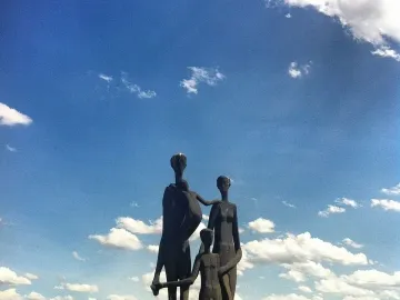 Dark bronze Monument to the Victims of Fascism sculpture of a family of five by the water under a blue sky.
