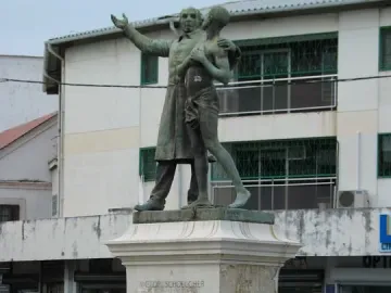 Victor Schœlcher statue with two bronze figures on a tall white pedestal at an urban intersection.