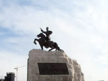 Statue of Damdin Sükhbaatar on a stone plinth with people posing on the steps below it.