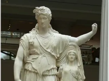 Hope Dionysus, a marble statue of a male figure with a leafy wreath, draped tunic, and animal skin over his shoulder, stands beside a smaller draped female figure in a museum gallery.