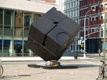 The Alamo black cube sculpture in a city street, with a person lying on its base.