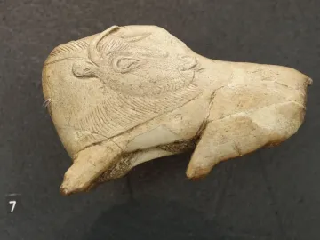 Carved bison figurine with its tongue extended, showing an engraved eye and textured fur details.