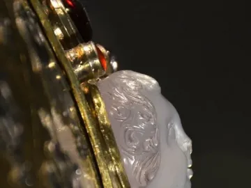 Close-up of Charlemagne\'s bust reliquary showing a carved light-colored cameo face set in ornate gold metalwork with red jewels.