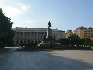 Tadeusz Kościuszko Monument standing on a tall pedestal in a paved square with a grand building behind it.