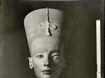 Black and white photograph of the Bust of Nefertiti, showing the crowned face, patterned collar, and a ruler for scale.