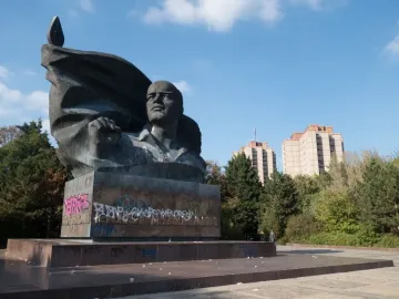Ernst Thälmann Memorial bronze bust on a graffiti-covered pedestal with a flag-like sculpture behind it.