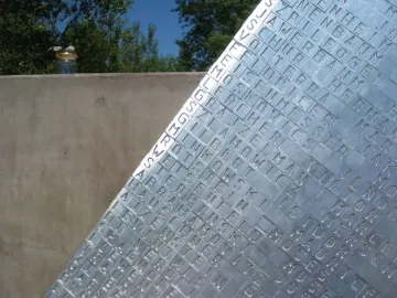 Hailfingen-Tailfingen Memorial panel with engraved names beside a concrete wall and a small jar of stones
