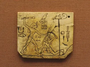 MacGregor plaque showing a crowned figure with a mace about to strike a kneeling figure, with hieroglyphs on the ivory surface.