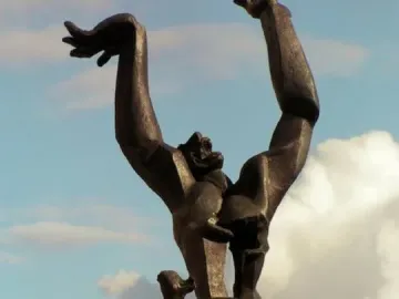 The Destroyed City bronze sculpture with raised arms and a hollow chest against a cloudy blue sky.