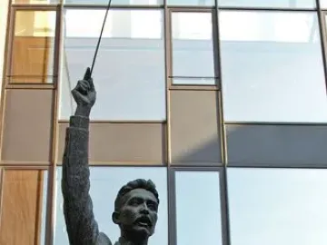 A Lluís Millet bronze statue holding a conductor’s baton aloft on a stone pedestal.