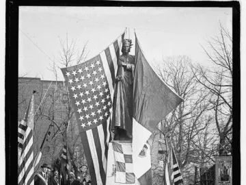 Crowned bronze statue of Dante Alighieri on a granite pedestal, with flags, wreaths, and people gathered below, including two children in the foreground.