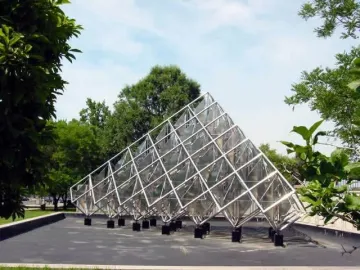 Delta Solar sculpture with reflective diamond-shaped panels and silvery metal framing outdoors among trees.