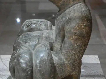 Las Limas Figurine showing a stone figure cradling a smaller carved figure with a stylized face and closed eyes.