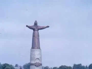 Mother Patroness monument in Cheboksary, a robed bronze figure with outstretched arms atop a tall pillar above landscaped steps and lawns.