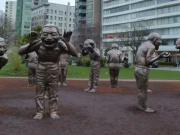 A-maze-ing Laughter sculpture with dark metallic laughing figures in a semicircle outdoors.
