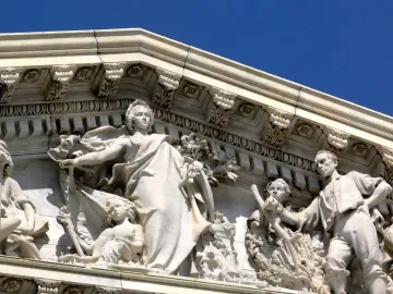 White marble pediment sculpture from Apotheosis of Democracy showing a crowned female figure with a torch beside smaller classical figures.