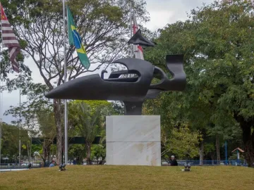 Ayrton Senna Monument on a grassy mound with a dark abstract race car-like sculpture and Brazilian flags behind it.