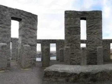 Maryhill Stonehenge replica with a circular arrangement of large grey stone pillars and openings, with distant hills and water visible through the structure.