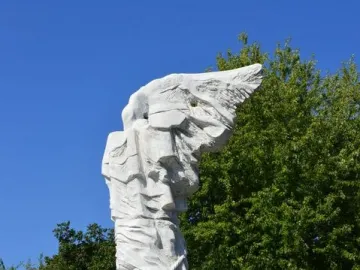 Monument to the Battle of Monte Cassino, a white marble abstract winged figure bound to a tall column in a garden.