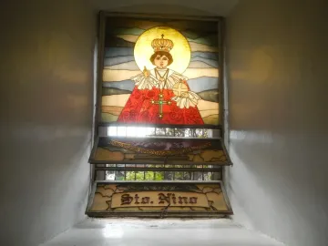 Stained glass depiction of Santo Niño de Cebú wearing a crown and red robes, holding an orb with a halo behind him.