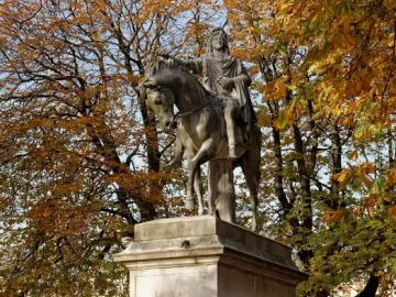 Equestrian statue of Louis XIII on a stone pedestal, surrounded by a black fence and autumn trees.