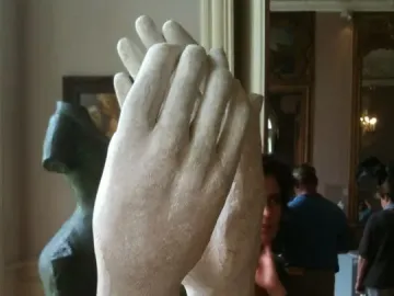 The Cathedral sculpture by Rodin, showing two clasped hands rising from a rectangular base in a museum setting.