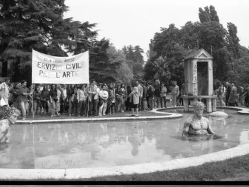 The Mystery Baths sculpture with two partially submerged statues in a pond, including a leaf-crowned head and a muscular male torso.