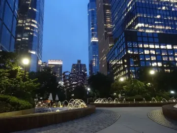 The Vessel partially visible among trees and illuminated skyscrapers at twilight.