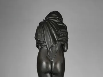 Rear view of Winter, a dark bronze female figure draped in heavy fabric and standing on a circular base.