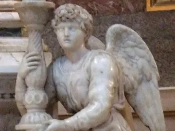 Angel sculpture kneeling and holding an ornate candlestick, with flowing robes and curly hair.