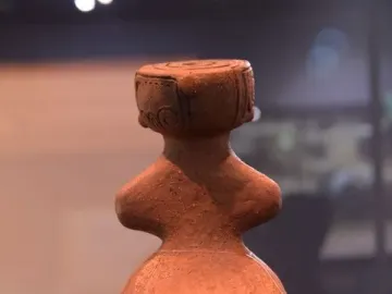 Rear view of the Jōmon Venus clay figurine with a broad rounded lower body and flat-topped head.
