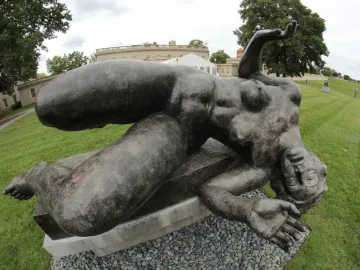 La Rivière by Aristide Maillol, a dark reclining female sculpture on a stone base in a garden setting.