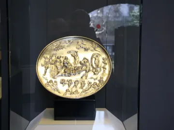 The Parabiago Plate displayed upright in a museum case, showing a detailed high-relief mythological scene on a circular metal dish.